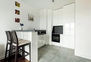 A modern kitchen with white cabinets, a black oven, and a dining area with two chairs.