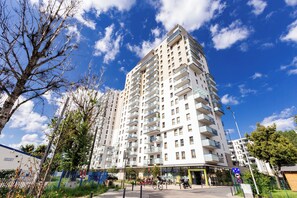 A multi-story residential building with balconies, a pedestrian walkway, and a clear blue sky.