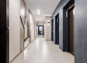 A modern hallway with a light-colored floor, dark walls with geometric patterns, and doors leading to rooms.