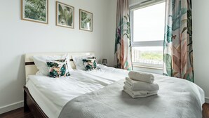 Ein Hotelzimmer mit Bett, Kissen, einem Fenster mit Vorhängen und gerahmten Bildern an der Wand.