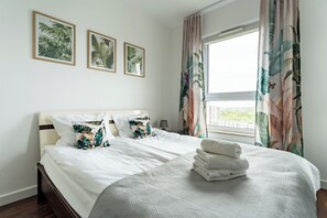 Ein Hotelzimmer mit Bett, Kissen, einem Fenster mit Vorhängen und gerahmten Bildern an der Wand.