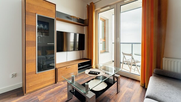 Ein modernes Wohnzimmer mit Glastisch, Holzschrank, Flachbildfernseher und einem Balkon mit Blick.
