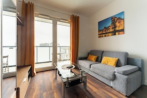 A modern living room with a grey sofa, a glass coffee table, and a painting of a castle on the wall.