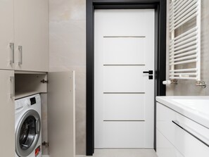Uma casa de banho moderna com porta branca, máquina de lavar embutida e suporte para toalhas.