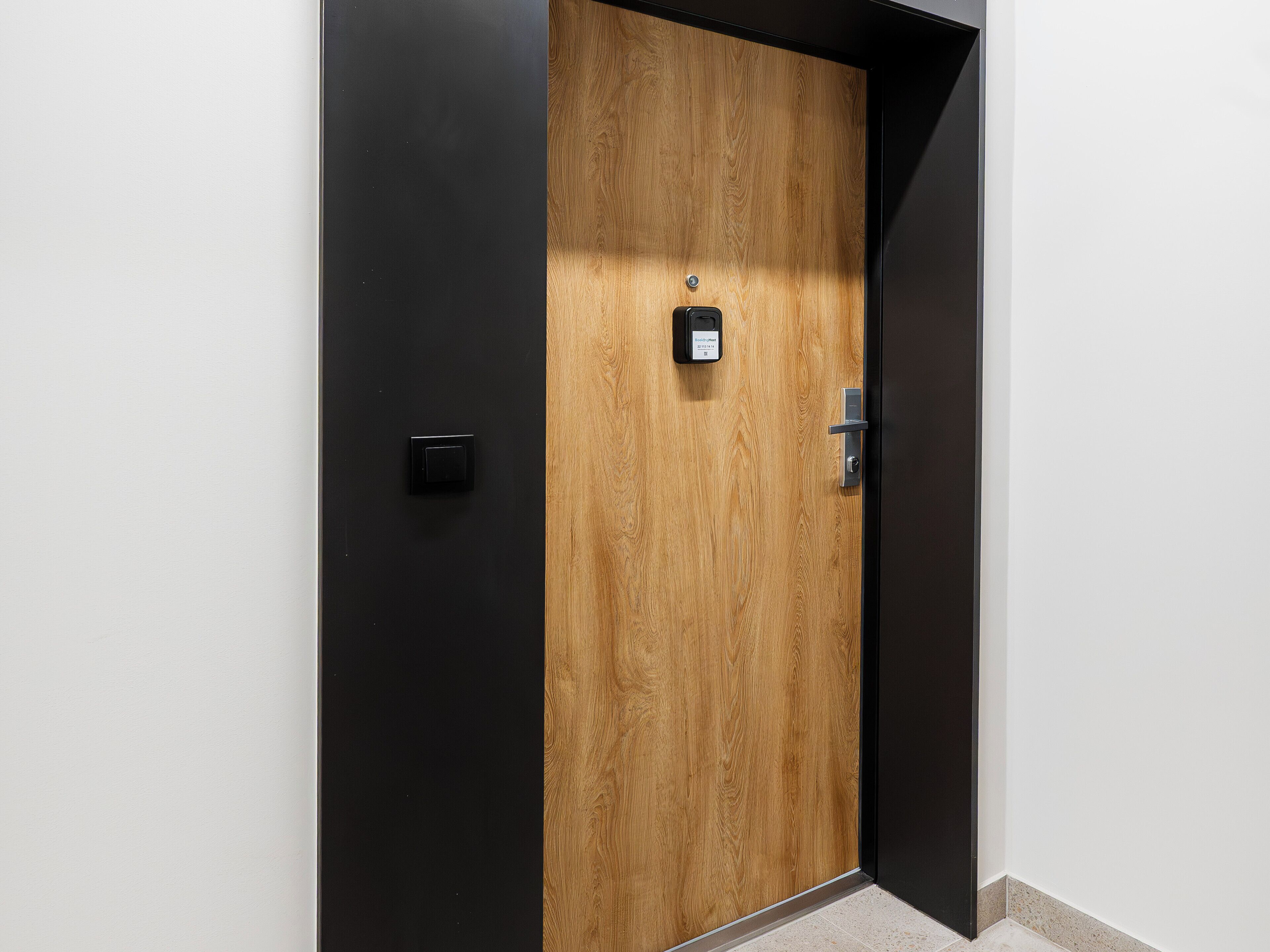 A wooden door with a black panel, a doorbell, and a door handle.