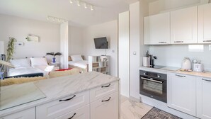Een moderne hotelkamer met een bed, nachtkastje, televisie en een kitchenette met een kookplaat en oven.