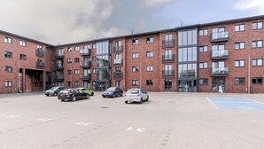 Een meerlaags gebouw met een bakstenen gevel, grote ramen en een parkeerplaats met aanduidingen.