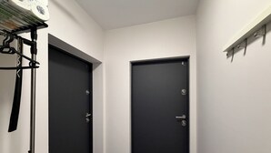 Een smalle gang met twee zwarte deuren, een witte muur en een plank met spullen aan de rechterkant.