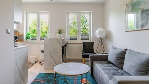 Ein modernes Wohnzimmer mit einem grauen Sofa, einem runden Couchtisch und Blick ins Freie durch große Fenster.