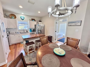 Una cocina con armarios blancos, una isla central y un comedor con mesa y sillas de madera.