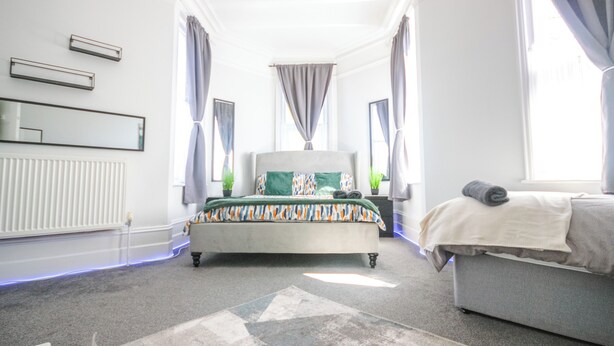 A bedroom with a bed, a sofa, a radiator, a mirror, and curtains. - Spacious Apt with Free Parking (Folkestone)