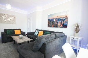 A living room with a sofa set, a coffee table, a world map on the wall, and a cityscape painting. - Spacious Apt with Free Parking (Folkestone)