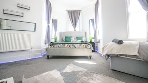A bedroom with a bed, a sofa, a radiator, and a window with curtains. - Spacious Apt with Free Parking (Folkestone)