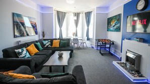 A modern living room with a sofa, coffee table, and a fireplace. There is a foosball table and a flat-screen TV mounted on the wall. - Spacious Apt with Free Parking (Folkestone)