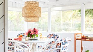 Un coin repas avec une table blanche, des chaises en osier et un luminaire suspendu en fibres tressées.