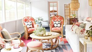 Une pièce spacieuse avec une grande fenêtre, des meubles en osier, un tapis à motifs et un canapé blanc.