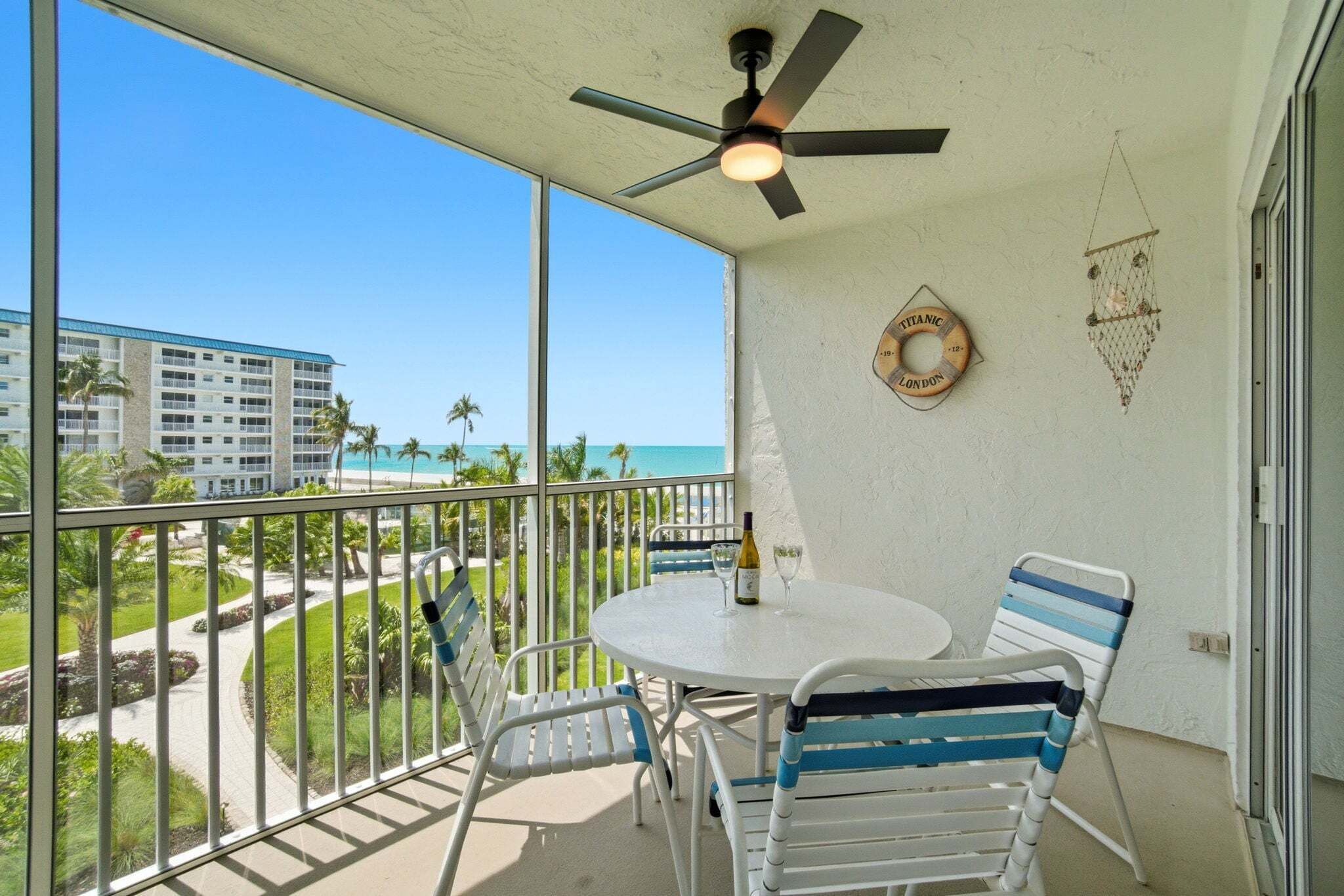 A balcony with a table and chairs, a ceiling fan, and a view of the ocean and hotel buildings.