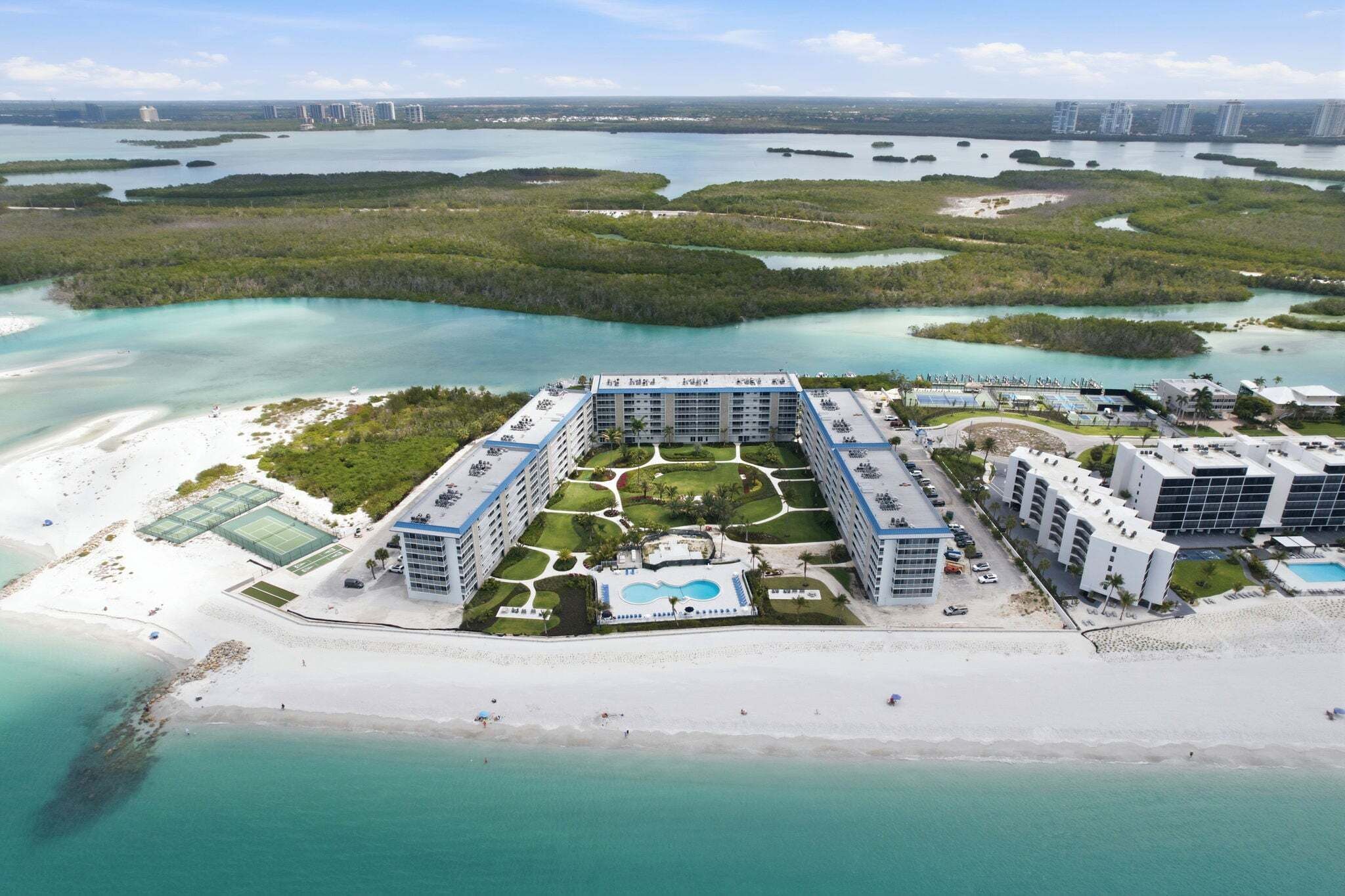 Ein Resort mit mehreren Gebäuden, einem Schwimmbad, Tennisplätzen und einem Strand.