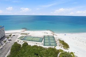 A beachside hotel with multiple tennis courts, a parking area, and a view of the ocean. - Beachfront Retreat • Pool • Pickleball • Sleeps 6 (Bonita Springs)