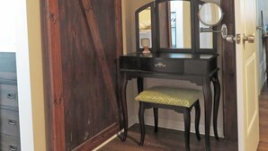 Ein Zimmer mit Holzboden, einem dunklen Holzschreibtisch mit Spiegel, einer Bank und einer Tür mit Schiebetür-Mechanismus im Scheunenstil.