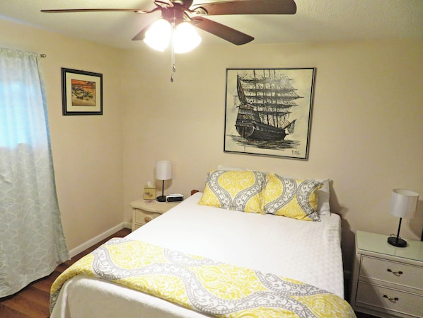 Ein Schlafzimmer mit Bett, Nachttisch, Lampe, Deckenventilator und einem Wandbild eines Schiffes.