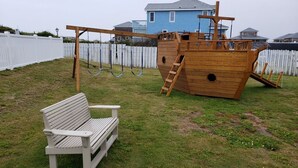 Een houten speelconstructie in de vorm van een schip met een bankje in een gazon.