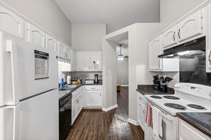 Una cocina con armarios blancos, un refrigerador, una estufa y una cafetera.