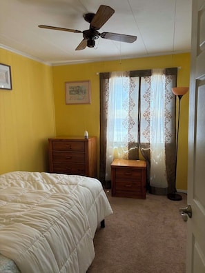 A bedroom with a bed, a dresser, a nightstand, a ceiling fan, and a window with curtains.