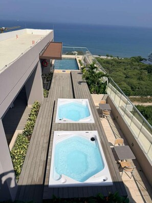 Eine Dachterrasse mit zwei Whirlpools und einem Pool mit Blick auf die Küste.