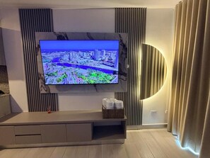A modern living room with a large flat-screen TV mounted on a wall, a minimalist entertainment unit below, and a decorative wall panel. - Santa Marta Apartment with Ocean Views (Santa Marta)