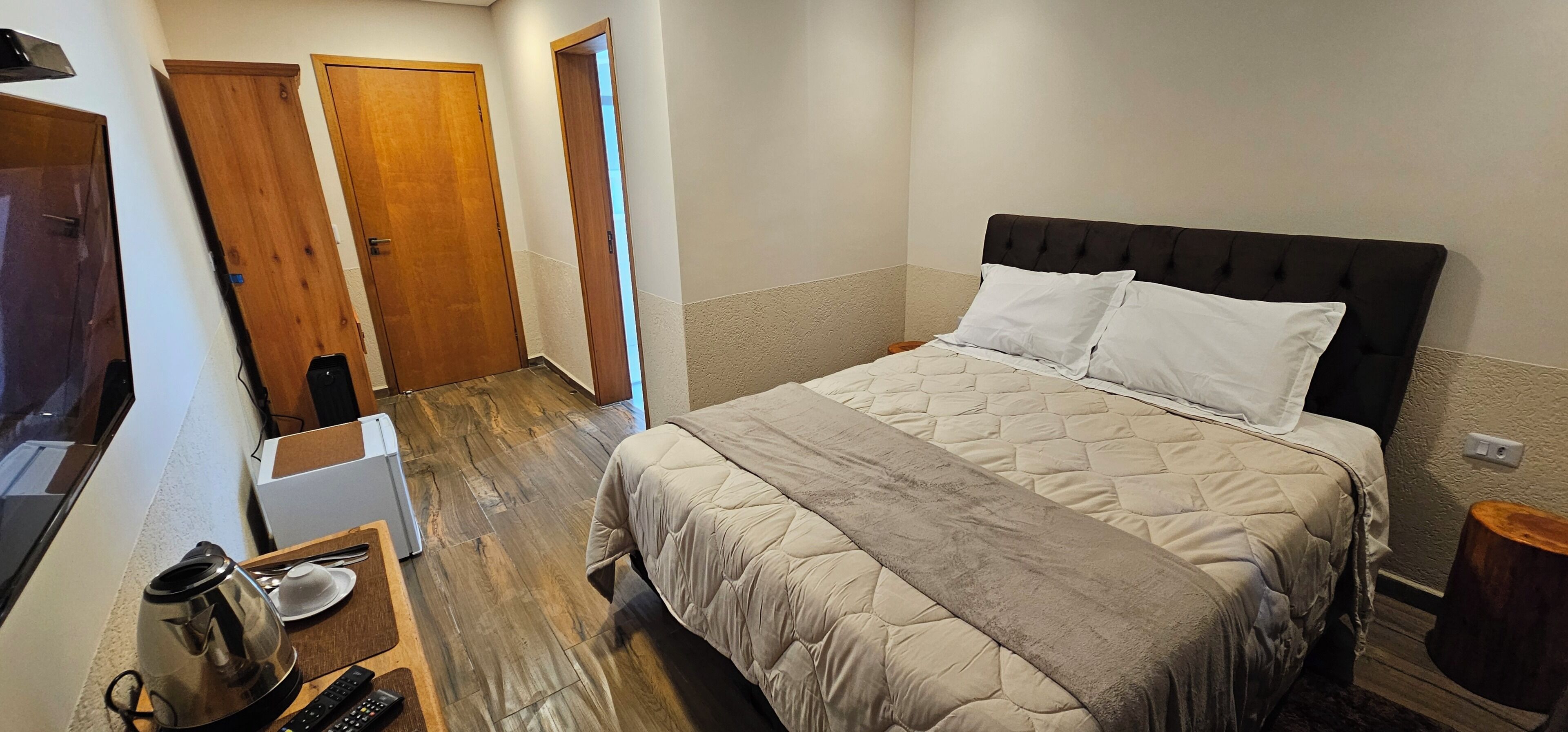 Een slaapkamer met een bed, een nachtkastje met een waterkoker, en een houten vloer.