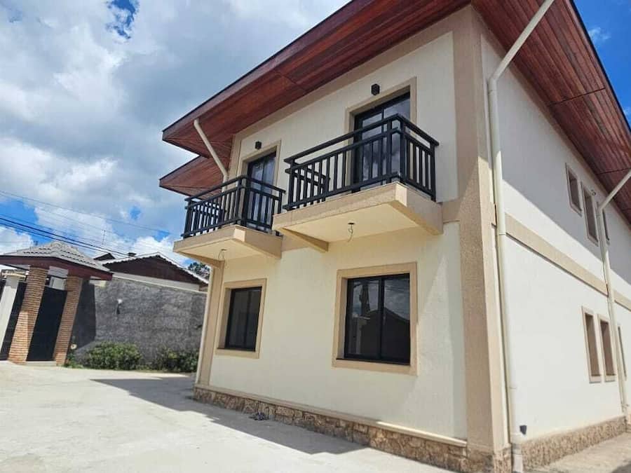 A two-story house with a balcony, a gated entrance, and a clear sky.