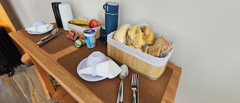 A wooden table with breakfast items, a thermos, and a basket of bread.