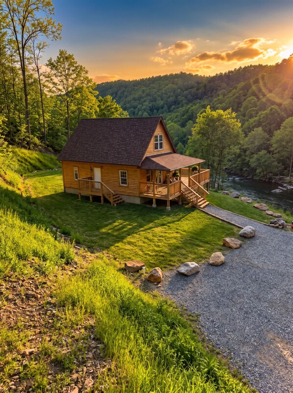 Una cabaña de madera con un porche, una terraza y vistas a un río y bosque.