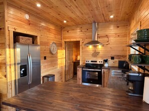 A compact kitchen with wooden walls, a stainless steel refrigerator, a stove, and a sink.