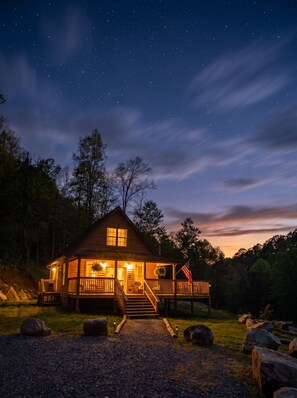 A wooden cabin with a porch, a flag, and a starry night sky.