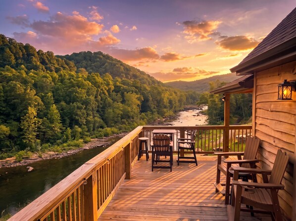 A wooden deck with outdoor seating overlooking a river and forested hills.