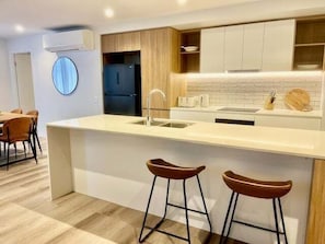 A modern kitchen with a central island, bar stools, and a dining area with chairs.