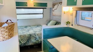 Un intérieur de camping-car compact comprenant un lit, un coin repas et une petite cuisine.
