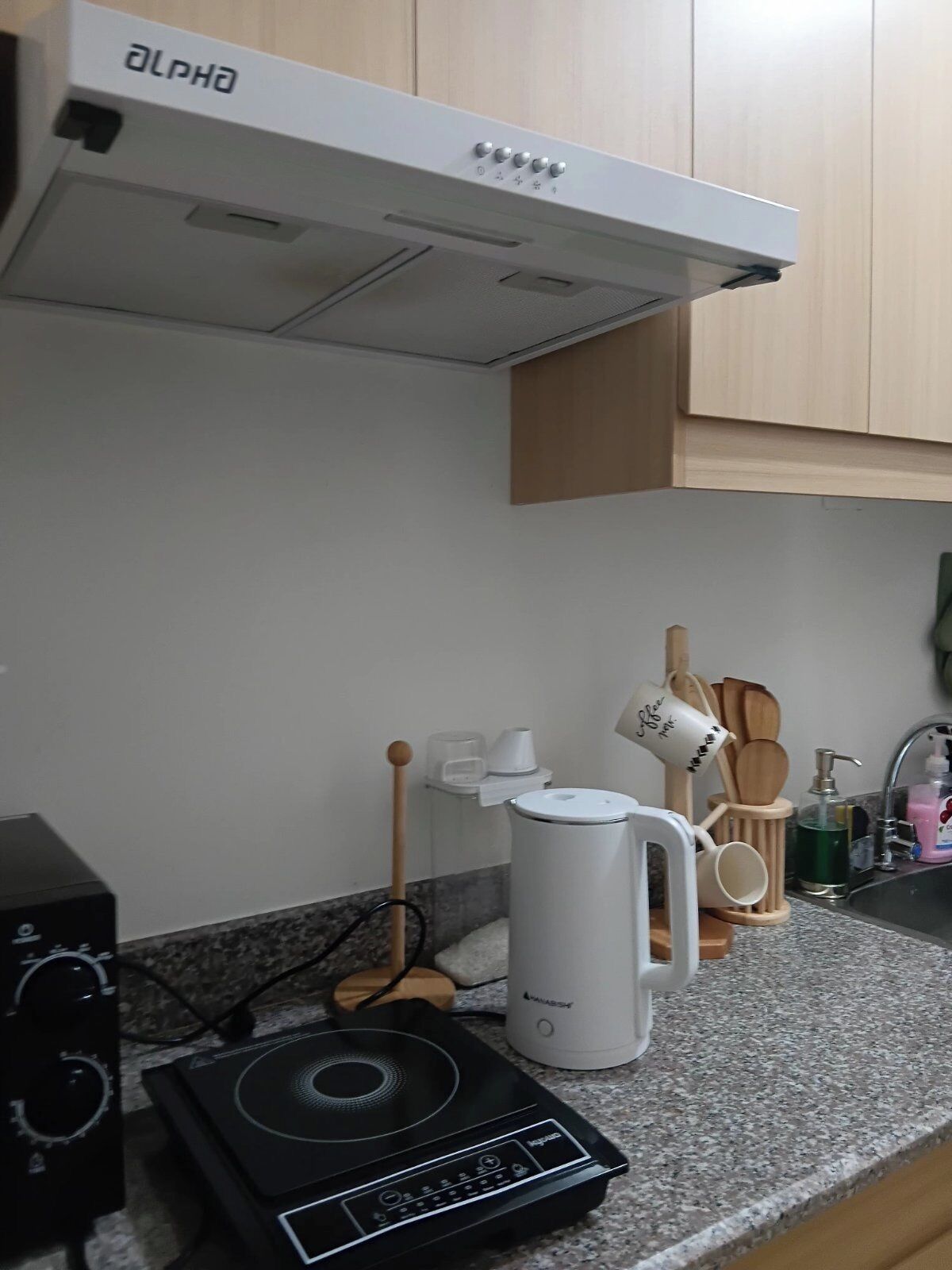 A kitchen with a coffee maker, a kettle, and a speaker on the counter.