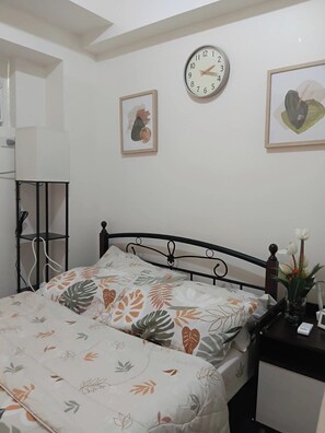 Ein Schlafzimmer mit einem Bett, einem Nachttisch mit Lampe, einer Uhr und gerahmten Bildern an der Wand.