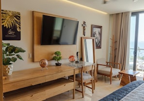Ein modernes Hotelzimmer mit einem Holztisch, einem Fernseher, einem Kruzifix und einem gerahmten Kunstwerk.