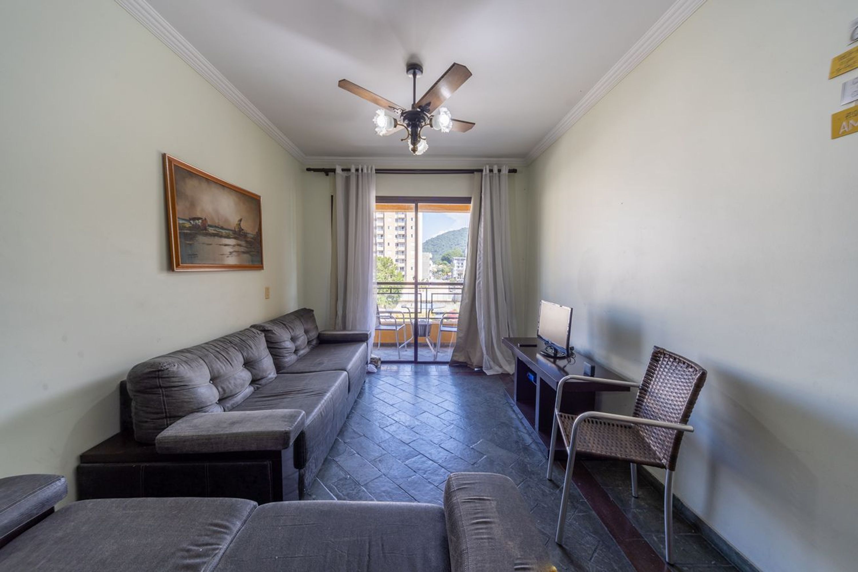 Ein Wohnzimmer mit einer Couch, einem Sessel, einem Deckenventilator, einem Gemälde und Blick durch eine Glastür.
