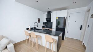 Una cucina moderna con un piano di lavoro nero, tre sgabelli da bar in legno, un forno a incasso e una porta bianca.