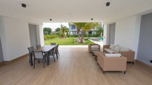Un'ampia zona giorno con tavolo e sedie, un divano e vista su piscina e giardino.