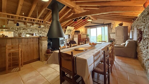 Eine rustikale Küche mit Steinwand, Holzbalken, einem großen Kamin und einer Essecke mit Tisch für vier Personen.