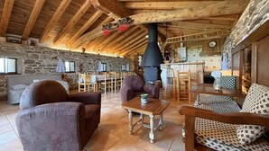 Ein rustikaler Innenraum mit Steinwand, Holzbalkendecke, Kamin und Essbereich.