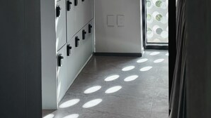 Een modern interieur met een wandlamp, een raam met patroon en een betegelde vloer.