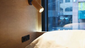 Een kamer met een houten wand, een raam en een bed met een wit laken.