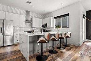 A modern kitchen with white cabinetry, a central island with bar stools, a microwave, and a large window. - South Austin Luxury: SoCo, S. 1st + Cowboy Pool (Austin)